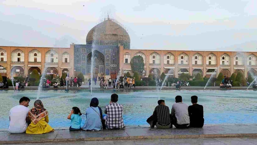 Iranian women and men sitting at teh fountain of the Naqsh-e Jahan square of Isfahan